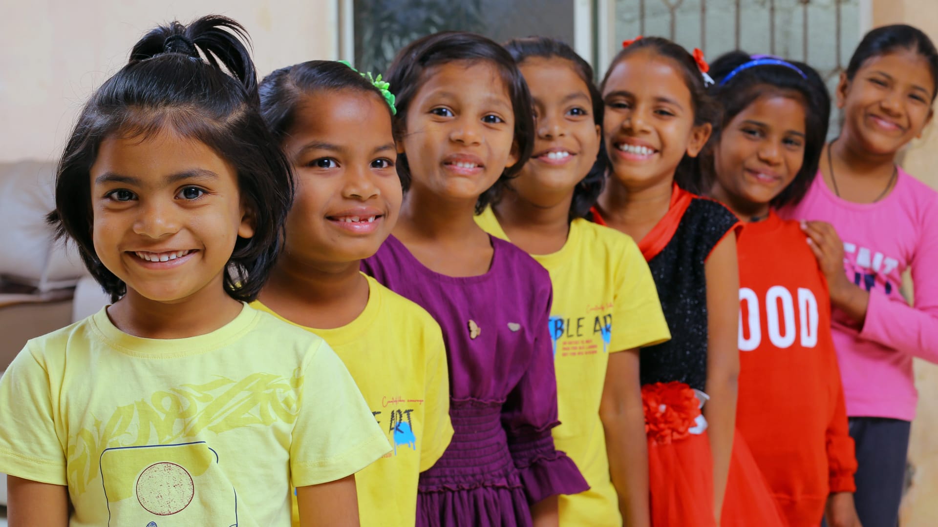 Seven girls from the Aadarana home standing in a line, smiling at the camera