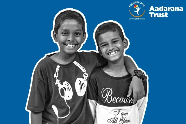 Two boys from the Aadarana homes with their arms around each other, laughing, on the trust's blue campaign field