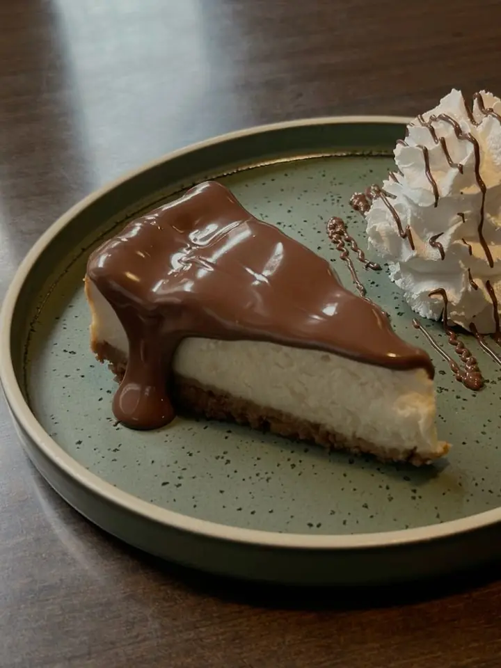 A slice of cheesecake under chocolate sauce on a green speckled plate